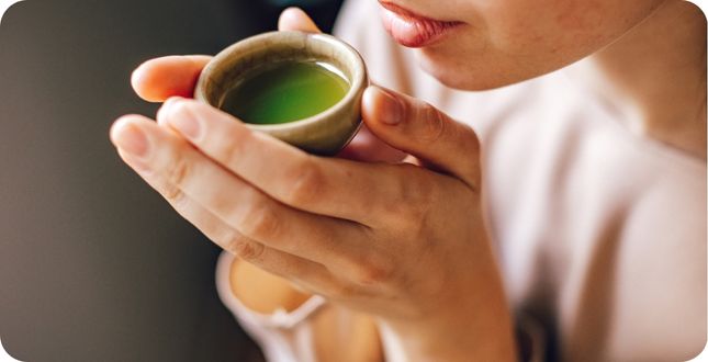 Vrouw drinkt een klein glaasje groene matcha thee.