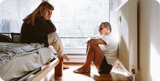 Man en vrouw in gesprek op de slaapkamer tijdens een midlife crisis, met zichtbare signalen van spanning en twijfel.