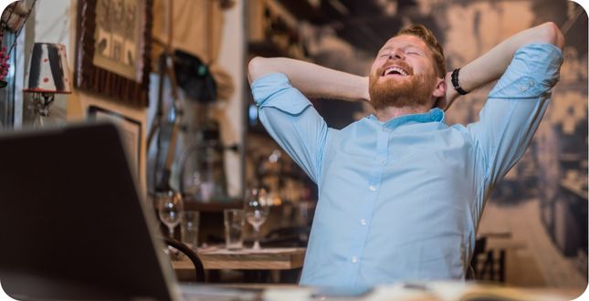 Man achteroverleunend en lachend in een café, symbool voor opluchting en herwonnen energie na een midlife crisis.