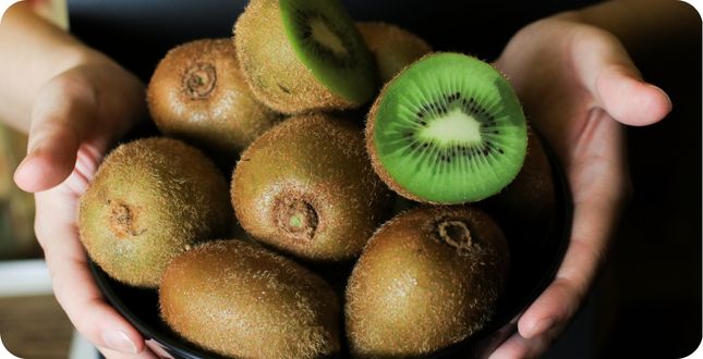 Kom met verse groene kiwi's, waarvan één kiwi doorgesneden om het heldergroene vruchtvlees te tonen.